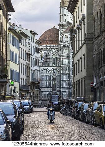 Stock Photograph - A motorcyclist on a cobblestone street with Florence Cathedral in the background; Florence, Italy. Fotosearch