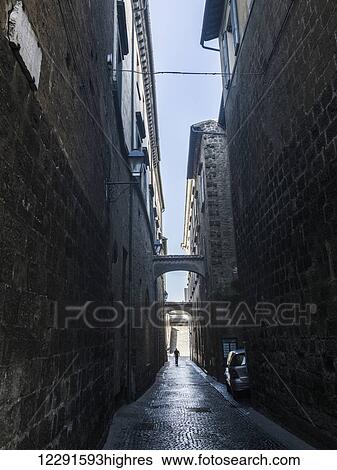 Stock Photograph - A narrow alley between two buildings with a view of blue sky; Orvieto, Umbria, Italy. Fotosearch