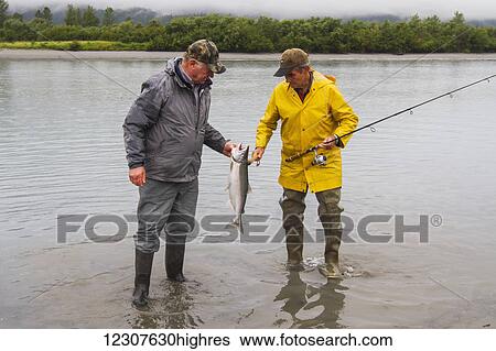 Stock Photograph - A pair of friends look at a freshly caught Silver Salmon from a stream in the Portage Valley in Summer. Southcentral Alaska.. Fotosearch