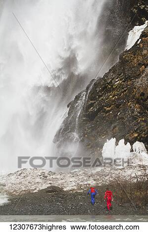 Stock Photograph - A pair of rafters walk towards Bridal Veil Falls near Valdez, Southcentral Alaska, USA. Fotosearch