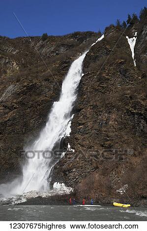 Stock Photograph - A raft stops at Bridal Veil Falls in Keystone Canyon near Valdez, Alaska in Spring. Southcentral Alaska.. Fotosearch