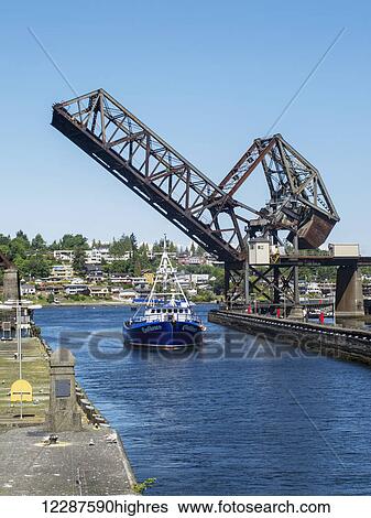 A ship in a canal drives under the raised bridge on a clear sunny day, Ballard Locks, Seattle, Washington, Summer, USA View Large Photo Image Stock Photograph - A ship in a canal drives under the raised bridge on a clear sunny day, Ballard Locks, Seattle, Washington, Summer, USA. Fotosearch