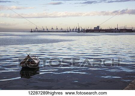 A small boat moored in the tranquil water wit cranes in the port in the distance at sunset; Thessaloniki, Greece View Large Photo Image Stock Photograph - A small boat moored in the tranquil water wit cranes in the port in the distance at sunset; Thessaloniki, Greece. Fotosearch