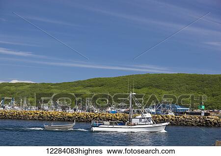Stock Photograph - A small fishing boat motors past a breakwater in Sand Point Harbor, Southwestern Alaska, USA, Summer. Fotosearch