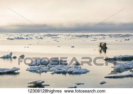 Stock Photograph - A small outboard boat motors through icebergs in the Arctic Ocean on a calm evening, 0rth Slope, Barrow, Arctic Alaska, USA, Summer. Fotosearch