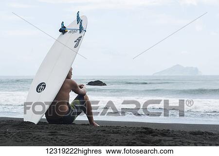 Stock Photograph - A surfer sits on the shore as he waits to get into the sea, Waiao beach, Yilan County; Taiwan, China. Fotosearch