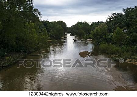 Stock Photograph - A tranquil river at sunset and a rider crossing on horseback in the distance; Yalepa, Jalisco, Mexico. Fotosearch