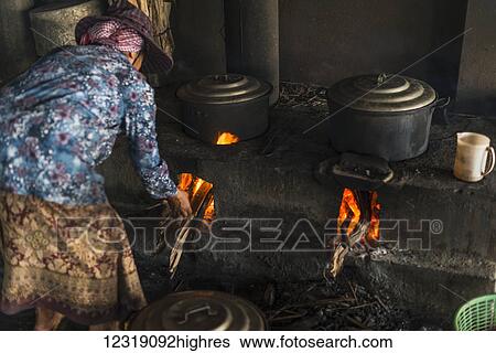 Stock Photograph - A woman puts firewood into the flames under pots, local life in the famous crab market; Kep, Cambodia. Fotosearch