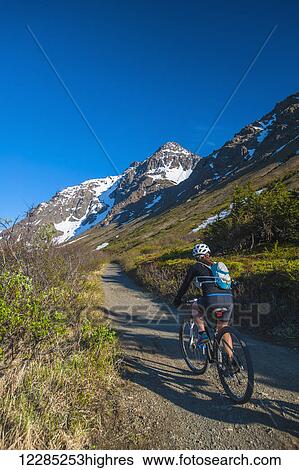 Stock Photograph - A woman riding her bike at Powerline Pass Valley in Chugach State Park, Southcentral Alaska.. Fotosearch
