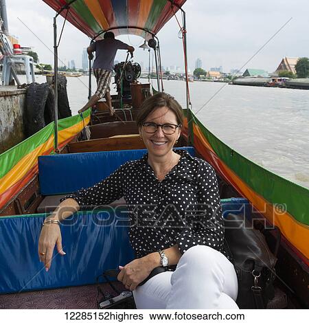 Stock Photograph - A woman sitting on a tour boat along the river's shore; Bangkok, Thailand. Fotosearch