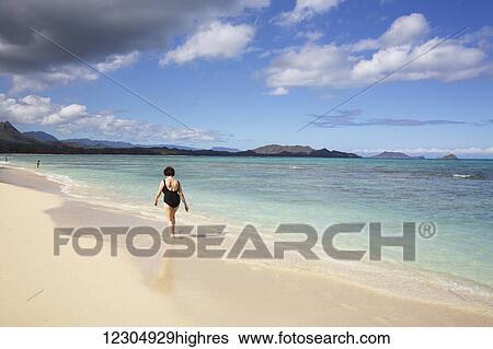Stock Photograph - A woman walks along the beach, Kaiona Beach Park; Waimanalo, Oahu, Hawaii, United States of America. Fotosearch