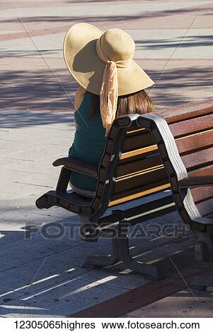 A woman wearing a wide brimmed hat sits on a wooden bench; Madrid, Spain View Large Photo Image Stock Photograph - A woman wearing a wide brimmed hat sits on a wooden bench; Madrid, Spain. Fotosearch