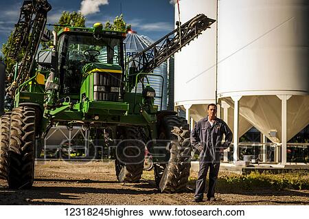 A young farmer stands posing beside a large tractor and grain storage bins on his farm; Herschel, Saskatchewan, Canada View Large Photo Image Stock Photograph - A young farmer stands posing beside a large tractor and grain storage bins on his farm; Herschel, Saskatchewan, Canada. Fotosearch