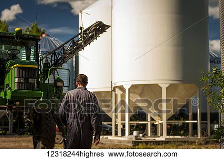 Stock Photograph - A young farmer walks towards a tractor and grain storage bins; Herschel, Saskatchewan, Canada. Fotosearch