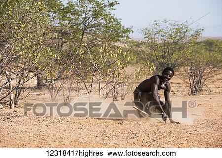 Stock Photograph - A young man from tourist attraction replica of Damara village is showing hunting traditions at the The Living Museum of the Damara; Namibia. Fotosearch