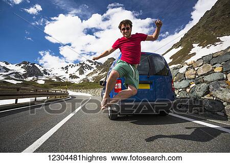 Stock Photograph - A young man jumps in the air on a mountain pass road in the Western Alps; Italy. Fotosearch