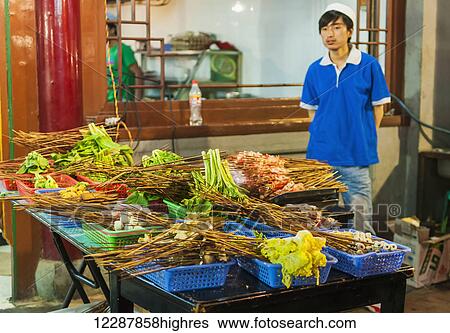 Stock Photograph - A Young Man Waiting For Customers In His Traditional Muslim Street Barbecue; Xian, Shaanxi Province, China. Fotosearch