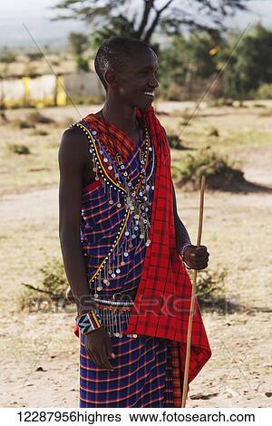 A young Masai man dressed in a traditional costume of blue, black and red checked clothing holds a stick in his hand and smiles as he talks; Narok, Kenya View Large Photo Image Stock Photograph - A young Masai man dressed in a traditional costume of blue, black and red checked clothing holds a stick in his hand and smiles as he talks; Narok, Kenya. Fotosearch