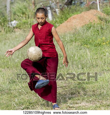 Stock Photograph - A young monk plays with a soccer ball; Punakha, Bhutan. Fotosearch