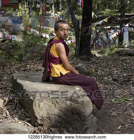 Stock Photograph - A young monk sitting on a rock; Paro, Bhutan. Fotosearch