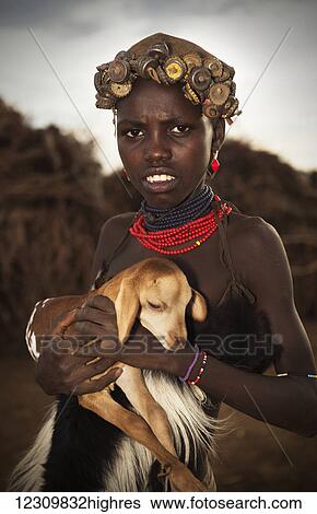 Stock Photograph - A young tribal woman holding a baby goat, Omo Valley; Ethiopia. Fotosearch