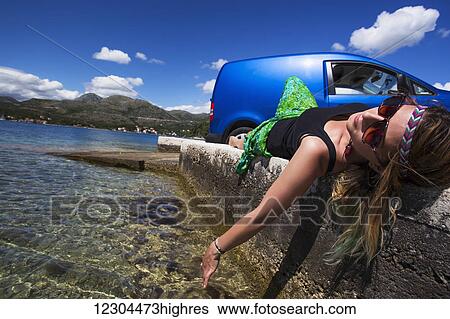 Stock Photograph - A young woman lays on a concrete wall at a beach along the coast; Slano, Croatia. Fotosearch