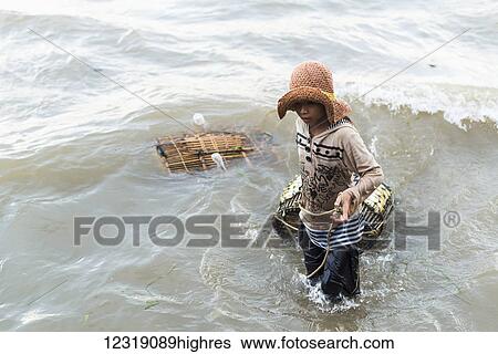 Stock Photograph - A young woman pulls crab traps from the water, local life in the famous Crab Market; Kep, Cambodia. Fotosearch