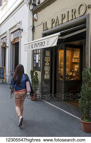 Stock Photograph - A young woman walks by a shop with a window display; Florence, Italy. Fotosearch