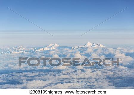 Stock Photograph - Aerial view of two snowcapped mountains in the Alaska Range peaking above the clouds, Anchorage, Southcentral Alaska, USA, Summer. Fotosearch