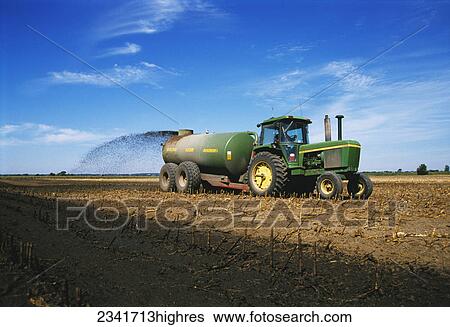Stock Photograph - Agriculture - A tractor and tank spreader spread liquid manure on a field of corn stubble for fertilizer / McHenry County, Illinois, USA.. Fotosearch
