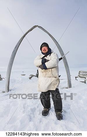 An Alaska native hunter wearing a white kuspuk and holding a rifle stands underneath the Browerville whalebone arch, Barrow, North Slope, Arctic Alaska, USA, Winter View Large Photo Image Stock Photograph - An Alaska native hunter wearing a white kuspuk and holding a rifle stands underneath the Browerville whalebone arch, Barrow, North Slope, Arctic Alaska, USA, Winter. Fotosearch