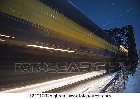 Stock Photograph - An Alaska Railroad train speeds by at night over a bridge near Talkeetna, Alaska.. Fotosearch