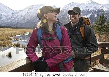 Stock Photograph - Backpacking couple looks out over the Eagle River Valley and Chugach Mountains from a viewing deck on the Rodak Nature Trail in Chugach State Park near the Eagle River Nature Center in Southcentral Alaska. Fotosearch