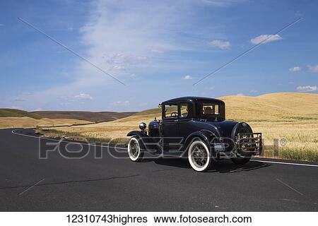 Stock Photograph - Black vintage car on a road winding between farm fields; Palouse, Washington, United States of America. Fotosearch