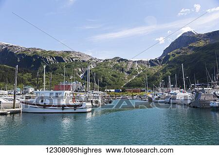 Stock Photograph - Boats docked at the Passage Canal Harbor in Prince William Sound, clear Sunny skies overhead, Whittier, South Central Alaska, USA, Summer. Fotosearch
