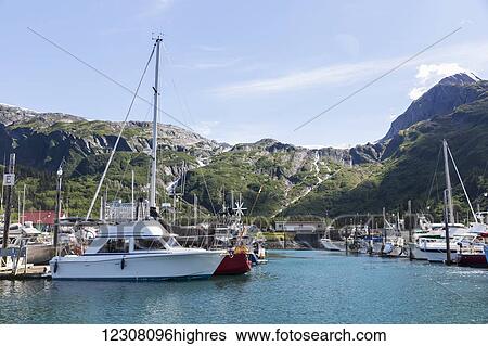 Stock Photograph - Boats docked at the Passage Canal Harbor in Prince William Sound, clear Sunny skies overhead, Whittier, South Central Alaska, USA, Summer. Fotosearch