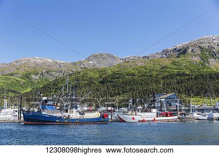 Stock Photograph - Boats docked at the Passage Canal Harbor in Prince William Sound, clear Sunny skies overhead, Whittier, South Central Alaska, USA, Summer. Fotosearch