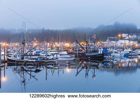 Stock Photograph - Boats in Ketchikan Harbor reflecting on the calm ocean waters on a foggy night, Ketchikan, Southeast Alaska. Fotosearch