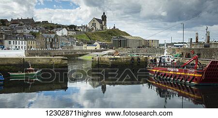 Boats in the tranquil harbour with colourful buildings on the hillside and a church on a hilltop; Aberdeenshire, Scotland View Large Photo Image Stock Photograph - Boats in the tranquil harbour with colourful buildings on the hillside and a church on a hilltop; Aberdeenshire, Scotland. Fotosearch