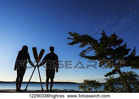 Boy and girl holding paddles overlooking Balsam Lake at sunrise; Ontario, Canada View Large Photo Image Stock Photograph - Boy and girl holding paddles overlooking Balsam Lake at sunrise; Ontario, Canada. Fotosearch