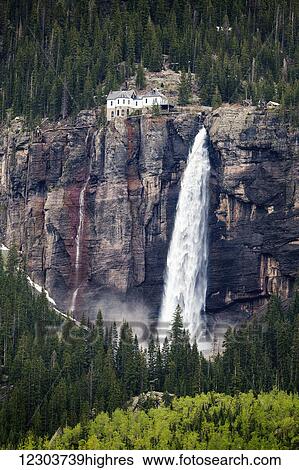 Stock Photograph - Bridal Veil Falls spilling out from the rocky cliff with an old building at the top, just beside the falls; Telluride, Colorado, United States of America. Fotosearch