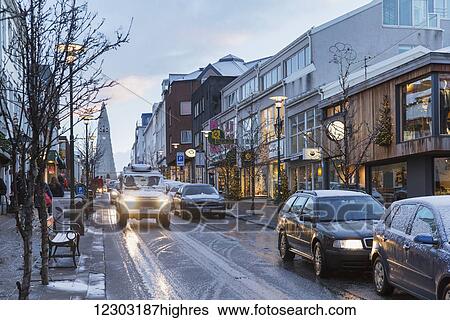 Stock Photograph - Cars driving down Laugavegur street in central Reykjavik during twilight in winter, Hallgrimskirkja in the background; Reykjavik, Iceland. Fotosearch