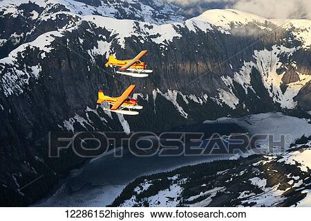 Stock Photograph - Cessna 185 flying in front of a DeHavilland Beaver and flying over rugged mountains and Manzoni Lake, Misty Fjords National Monument Wilderness, Spring. Fotosearch