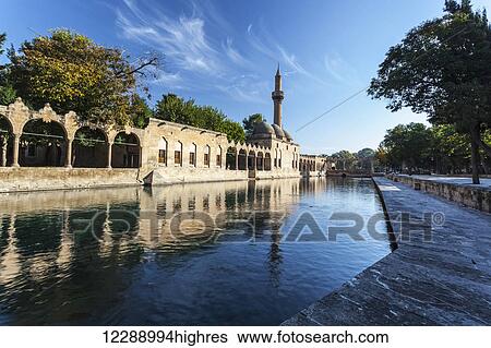 Stock Photograph - Chamber of Abraham and a minaret reflected in the tranquil water of a lake; Sanliurfa, Turkey. Fotosearch