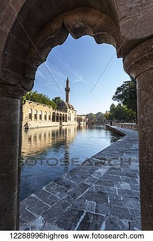 Stock Photograph - Chamber of Abraham and a minaret reflected in the tranquil water of a lake; Sanliurfa, Turkey. Fotosearch