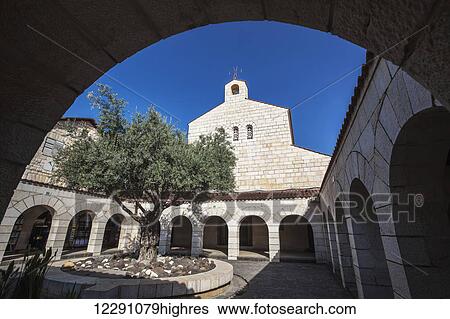 Stock Photograph - Church building with cross on top and a courtyard with a blue sky; Tabgha, Israel. Fotosearch