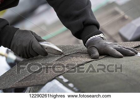 Stock Photograph - Close up of male roofer cutting new shingles with box-cutter knife; Calgary, Alberta, Canada. Fotosearch