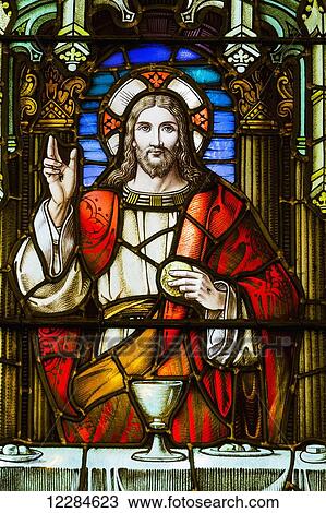 Stock Image - Close up of stain glass window with Jesus Christ at a table with chalice and holding bread; Calgary, Alberta, Canada. Fotosearch