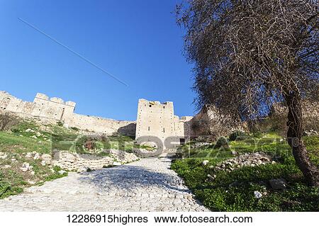 Stock Photograph - Cobblestone path leading to ruins and a blue sky; Corinth, Greece. Fotosearch