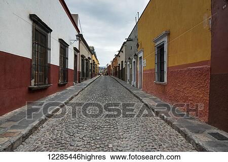 Stock Photograph - Cobblestone street between rows of buildings; San Miguel de Allende, Guanajuato, Mexico. Fotosearch